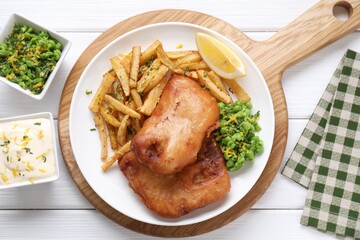 Tasty fish, chips, sauce, peas and lemon on white wooden table, top view