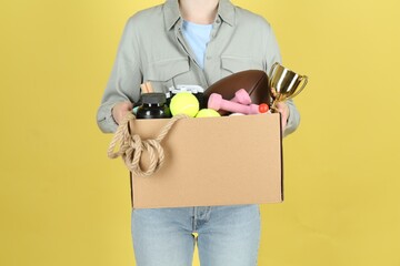 Woman holding box of unwanted stuff on yellow background, closeup