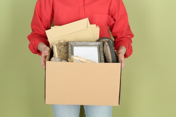 Woman holding box of unwanted stuff on green background, closeup - obrazy, fototapety, plakaty