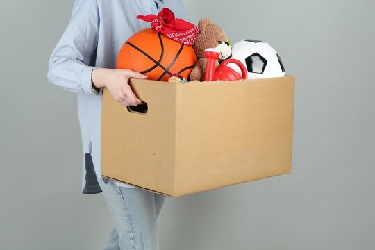 Woman holding box of unwanted stuff on grey background, closeup