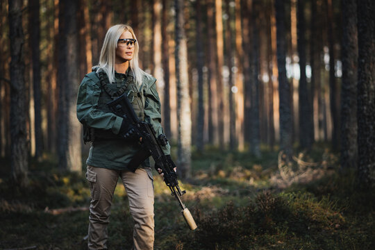 Beautiful military girl with a modern AK 12 suppressed rifle in the forest at war.