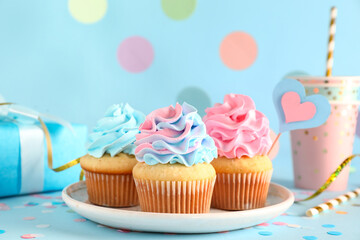 Plate with delicious cupcakes, gift box and decorations on blue background. Gender reveal party...