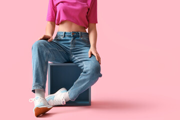 Young woman in stylish jeans pants sitting on pink background - Powered by Adobe