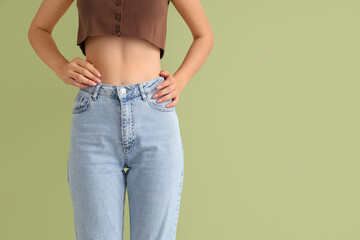 Young woman in stylish jeans pants on light green background