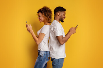 Couple back to back using smartphones on yellow - obrazy, fototapety, plakaty