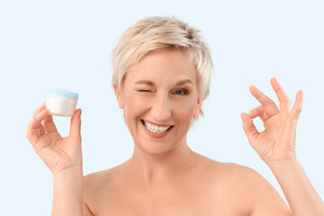 Mature woman with jar of anti-aging cream showing OK on blue background, closeup