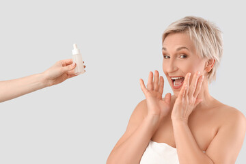 Surprised mature woman and hand with serum on light background, closeup