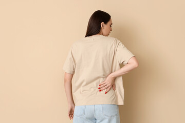 Young woman suffering from back pain on beige background