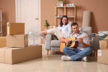 Happy young woman with her husband playing guitar in room on moving day