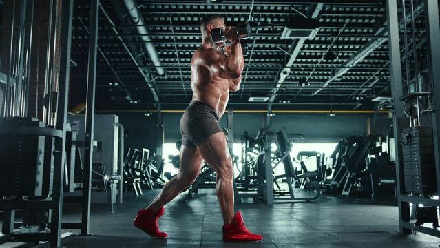 A man with well-defined muscles does dumbbell squats, demonstrating power and technique in his workout routine at a well-equipped gym. Camera 8K RAW. 