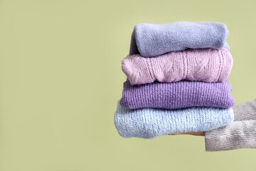 Woman with folded sweaters on green background