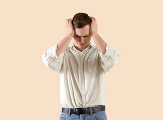 Young man suffering from headache on beige background