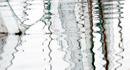 A fishing net in a river is reflected in an abstract pattern in the water