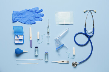 Gynecological speculum with stethoscope, pregnancy test and medical tools on blue background