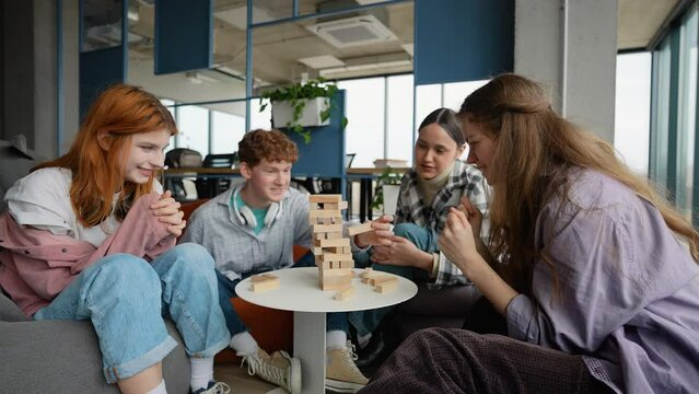 Young happy students spending free time in campus and playing Jenga. Teenagers friends playing a board game made of wooden rectangular blocks