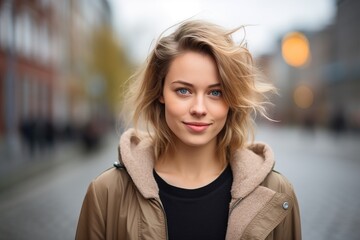 A woman with blonde hair and a tan coat is smiling for the camera
