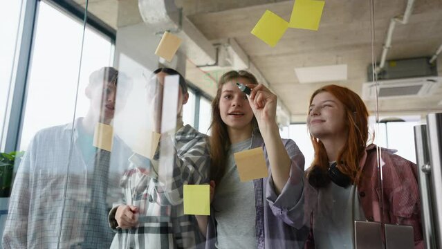 A group of students discussing a study plan and standing behind glass wall with sticky colorful papers