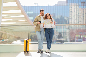 Loving couple holding map and using phone at airport