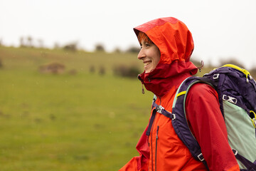 A woman wearing a red jacket and a blue backpack is smiling in the rain