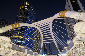 Chong Nonsi Skywalk - illuminated pedestrian walkway bridge arch - and skyscrapers in the downtown Central Business District (CBD) in Bangkok, Thailand, at dusk.