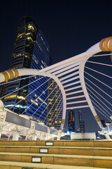 Chong Nonsi Skywalk - illuminated pedestrian walkway bridge arch - and skyscrapers in the downtown Central Business District (CBD) in Bangkok, Thailand, at dusk.