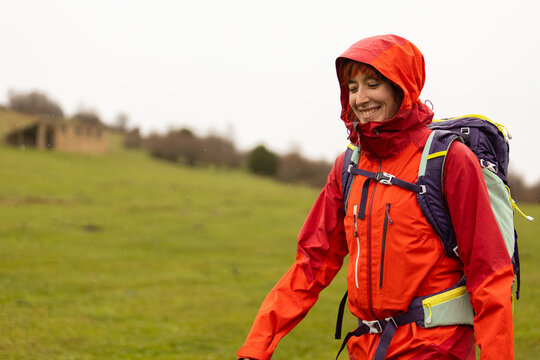 A woman wearing a red jacket and a backpack is walking in a field - Powered by Adobe