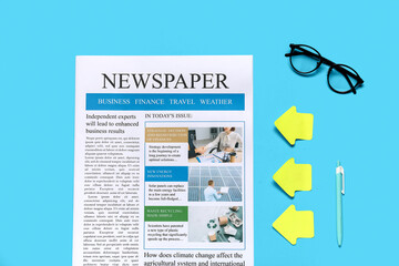 Newspaper with eyeglasses, stickers and pen on blue background