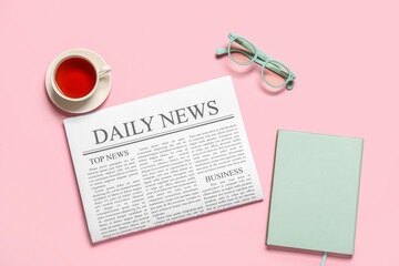 Newspaper with eyeglasses, notebook and cup of tea on pink background