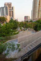 View of the empty and lush Chong Nonsi Canal Park and skyscrapers and other buildings in Khlong Chong Nonsi district in Bangkok, Thailand at day.