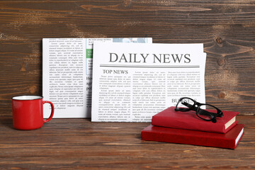 Newspapers with cup of tea, books and eyeglasses on wooden background