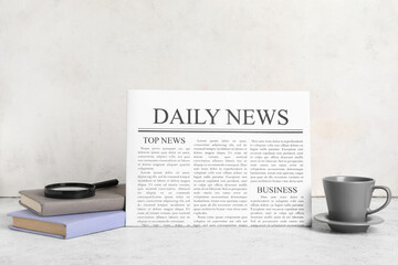Newspaper with cup of tea, books and magnifying glass on white grunge background