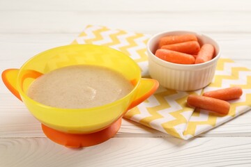 Baby food. Puree in bowl and small carrots on white wooden table