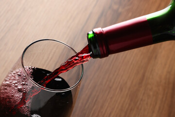 Pouring tasty red wine in glass at wooden table, closeup