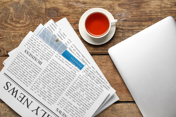 Newspapers with laptop and cup of tea on wooden background