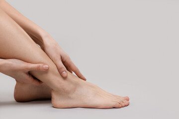 Woman suffering from leg pain on grey background, closeup. Space for text