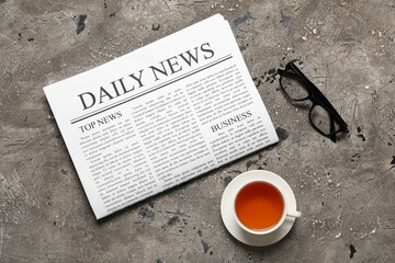 Newspaper with cup of tea and eyeglasses on grey grunge background