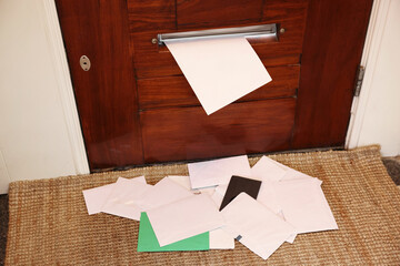 Wooden door with mail slot and many envelopes indoors
