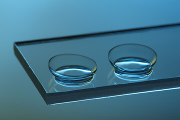 Pair of contact lenses on glass against light blue background, closeup
