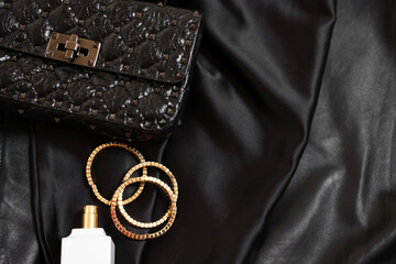 Leather bag, bottle of perfume and golden bracelets on black fabric, flat lay. Space for text