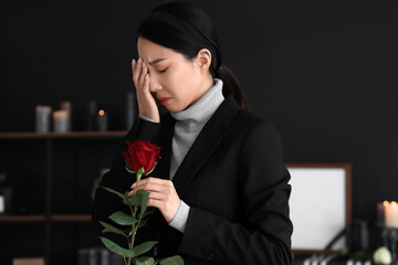 Mourning young Asian woman with rose at funeral