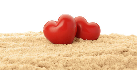 Fototapeta premium Honeymoon concept. Two red wooden hearts and sand isolated on white