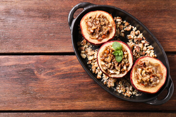 Fototapeta na wymiar Tasty baked apples with nuts, honey and mint in baking dish on wooden table, top view. Space for text