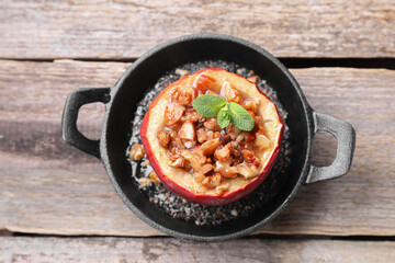 Tasty baked apple with nuts, honey and mint in baking dish on wooden table, top view