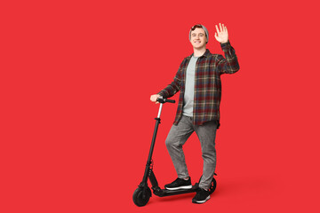 Young man with modern electric kick scooter on red background