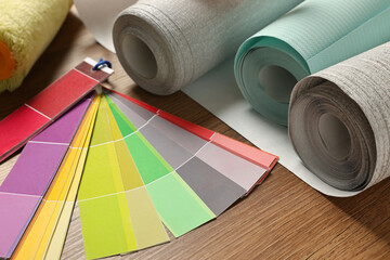 Different wallpaper rolls and color palette samples on wooden table, closeup