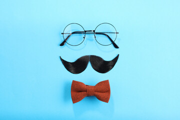 Artificial moustache, bowtie and glasses on light blue background, flat lay