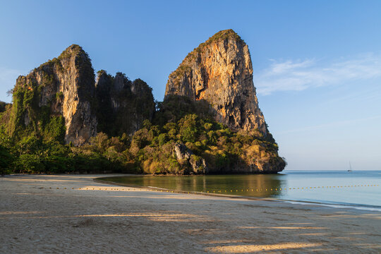 Scenic view of the empty Railay West beach and high limestone cliffs in Railay, Krabi, Thailand, on a sunny morning.