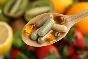 Different vitamin pills in spoon over fresh fruits, top view