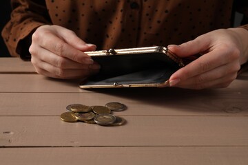 Poverty. Woman with empty wallet and coins at wooden table, closeup