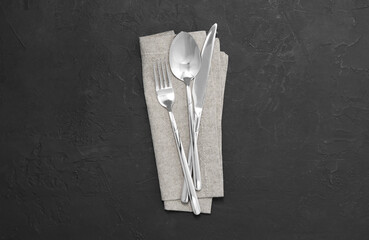 Beautiful cutlery set and kitchen towel on black table, top view